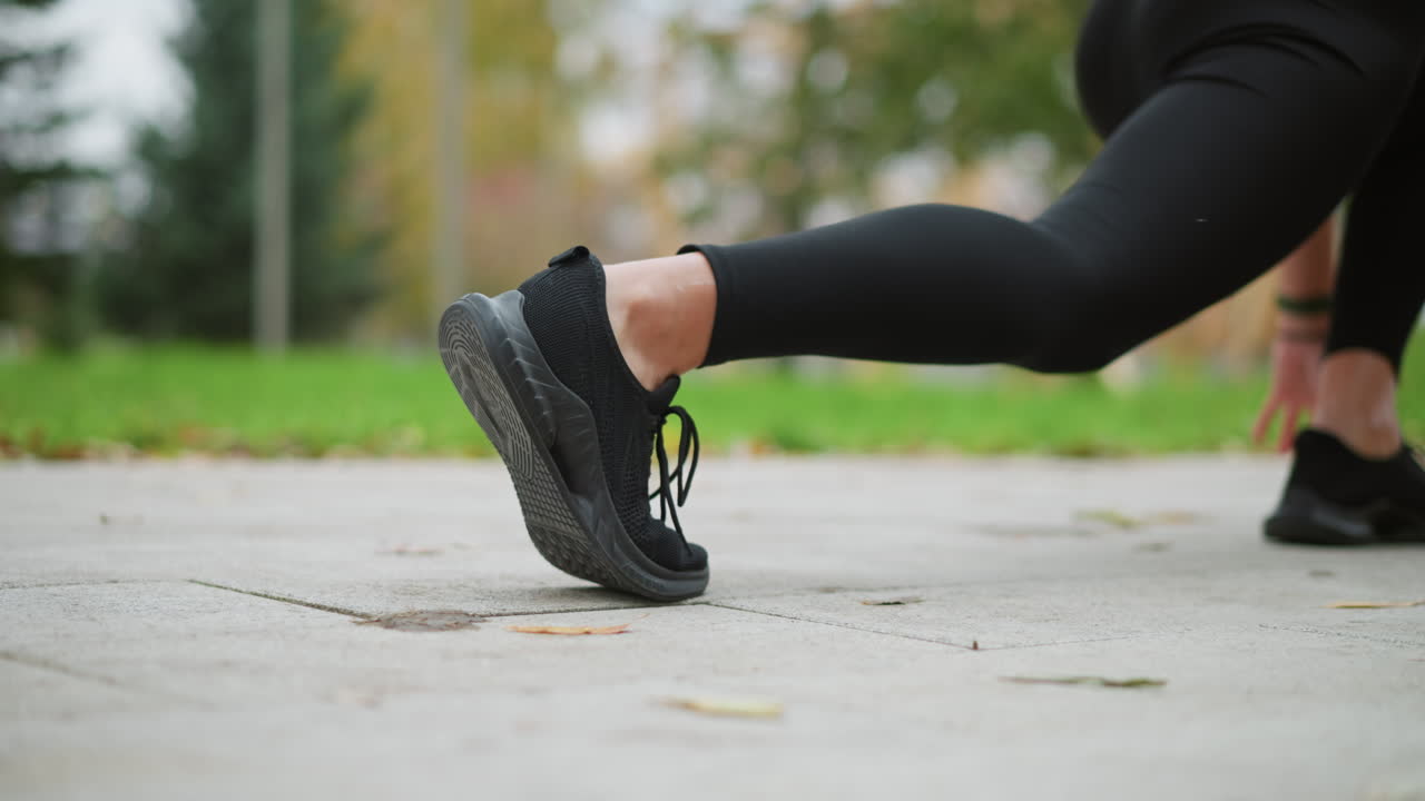 Close-up view of woman s leg set down in black sneakers, preparing to run, on paved path outdoors with natural blurred background, ready for an active workout or outdoor exercise