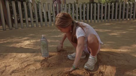 blonde girl plays in a sandbox square building a sand castle in summer