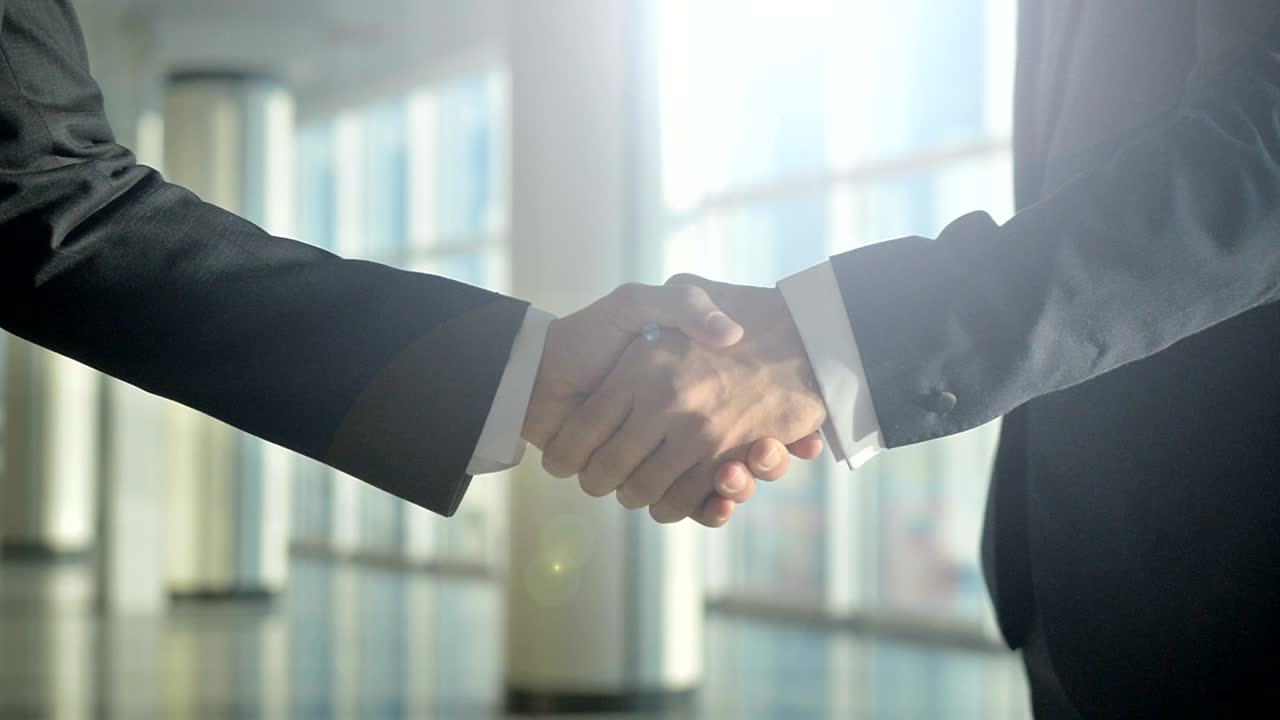 I due uomini d'affari si stringono la mano su uno sfondo soleggiato. Rallentatore