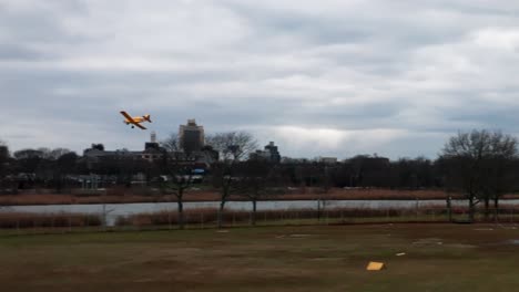 Un-Avión-De-Control-Remoto-Amarillo-Volando-En-Un-Parque-Con-Un-Lago-En-Un-Día-Nublado