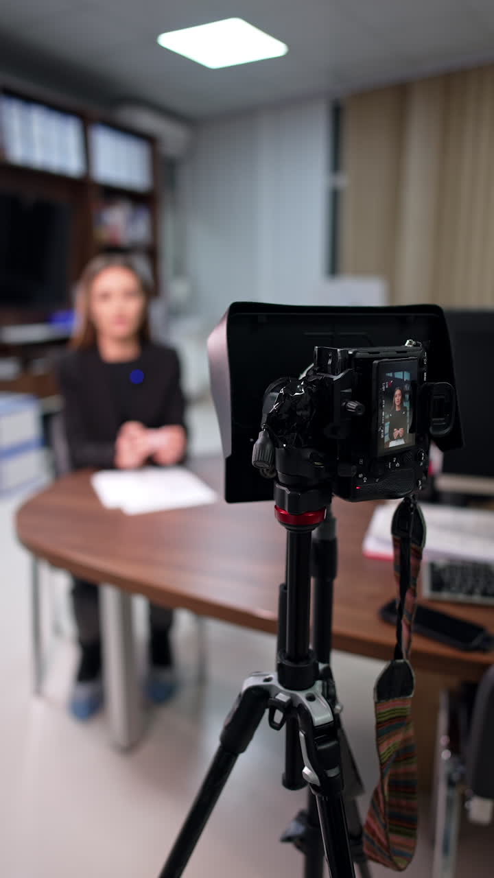 Blog content creation in the office. Unrecognized brunette woman talks to camera at blurred backdrop. Vertical video.