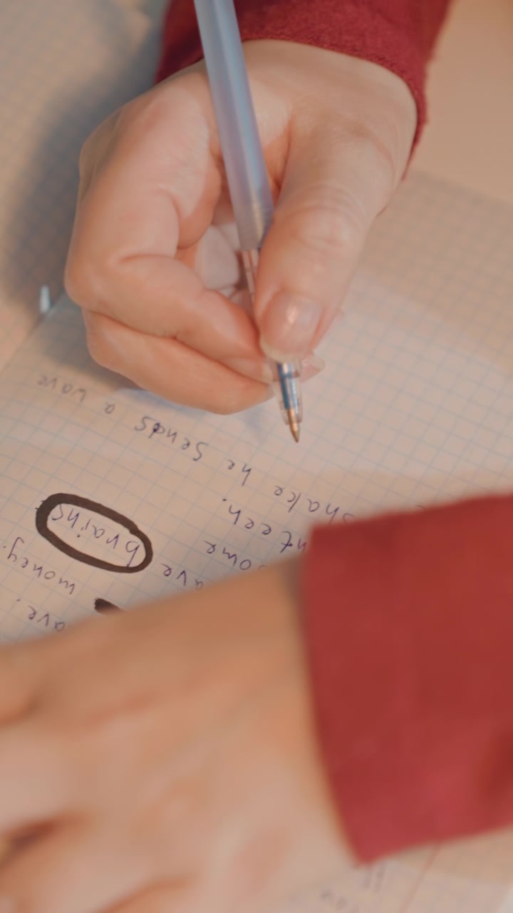 Nærbilde av en mann i røde ermer som skriver. Håndskriften inkluderer notater som «make man sends numbers 24031 427 90 money». Kameraet holder seg stabilt på hender og notatbok hele tiden