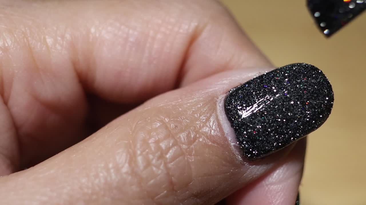 Close-up sequence of applying black glitter nail polish on a fingernail with precision.