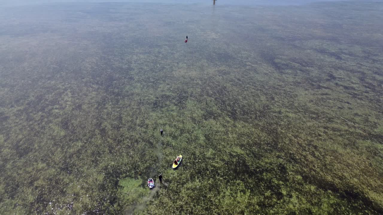4K drone pulls back from the horizon and pans down to reveal people kayaking in Mỹ Hòa Lagoon, Phan Rang. Stunning turquoise water and white sands under clear skies.