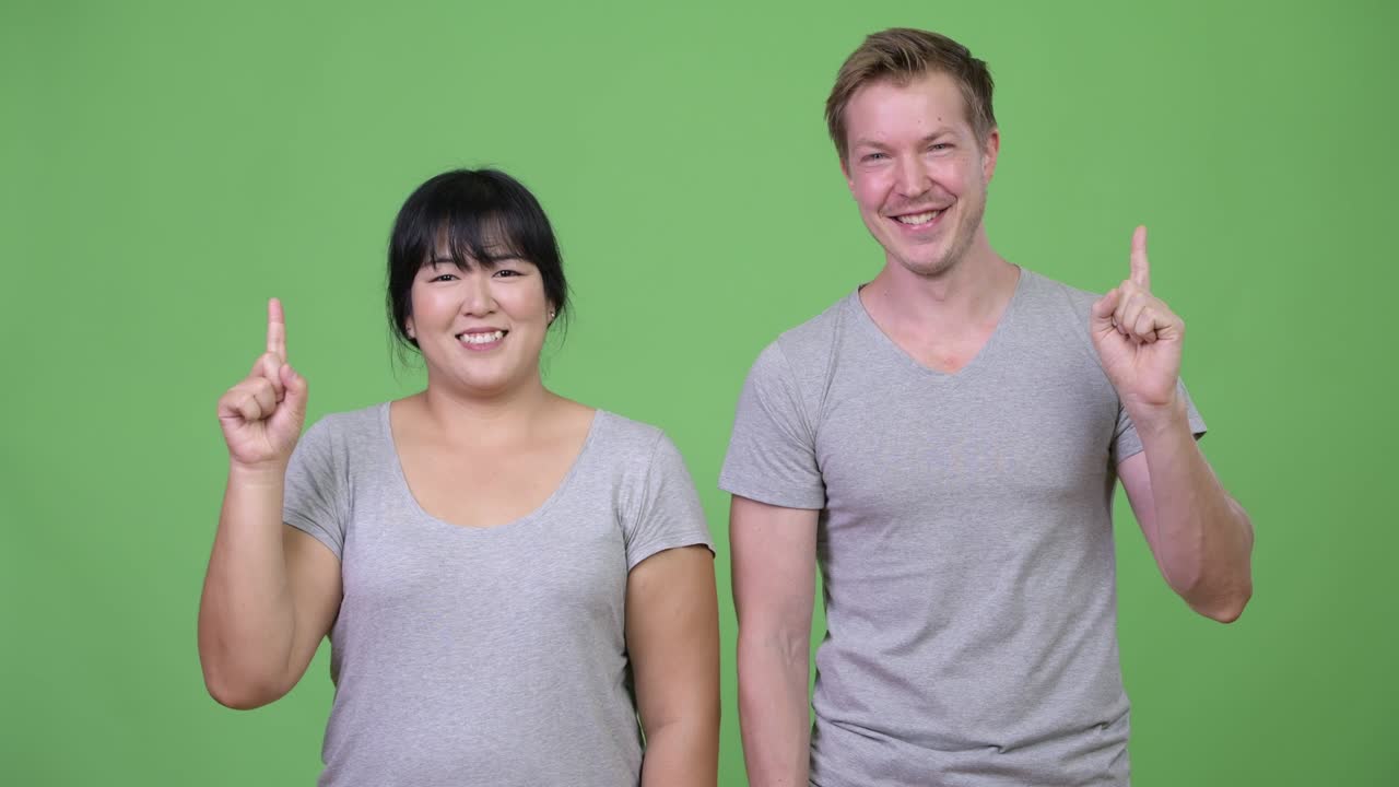 Young happy multi-ethnic couple pointing up together