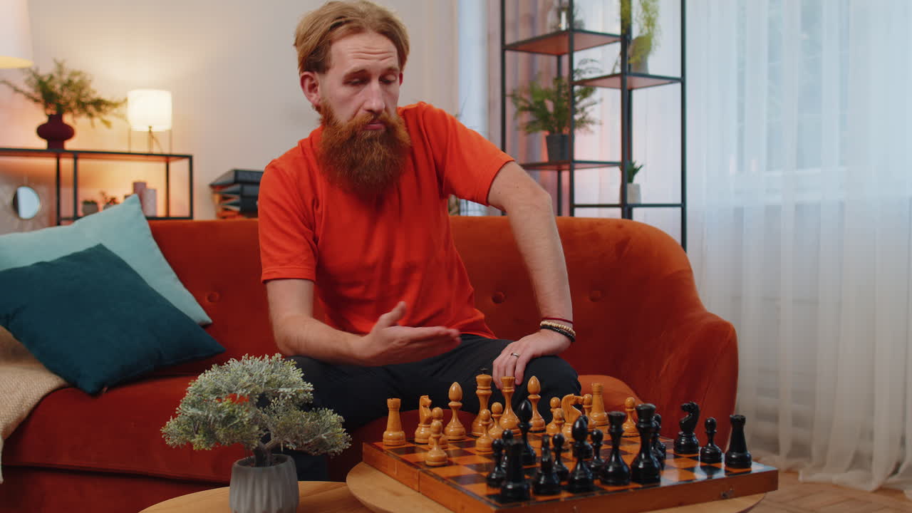 joven pelirrojo barbudo enfocado jugando al ajedrez juego de mesa de ocio solo, actividad doméstica en casa