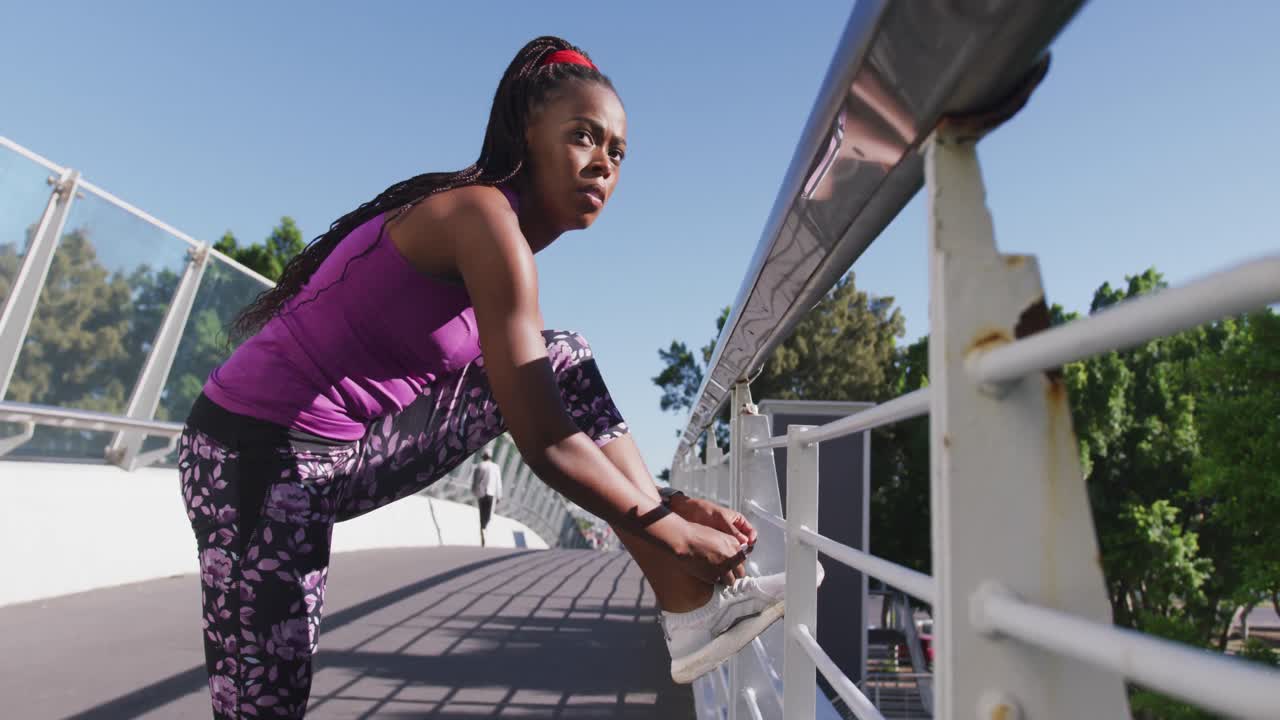 African american woman tying shoe laces on the railing of the city bridge