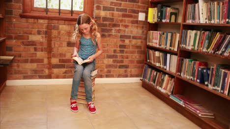 Cute-pupil-reading-while-sitting-on-pile-of-books