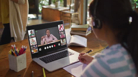 girl doing homework and having a video conference with teacher and classmates on laptop at home