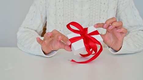 close up female hands tie the red bow of a gift box with white wrapping