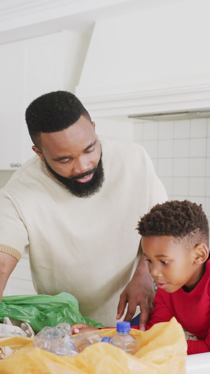 Vertical video of african american father and son sorting waste in kitchen, in slow motion