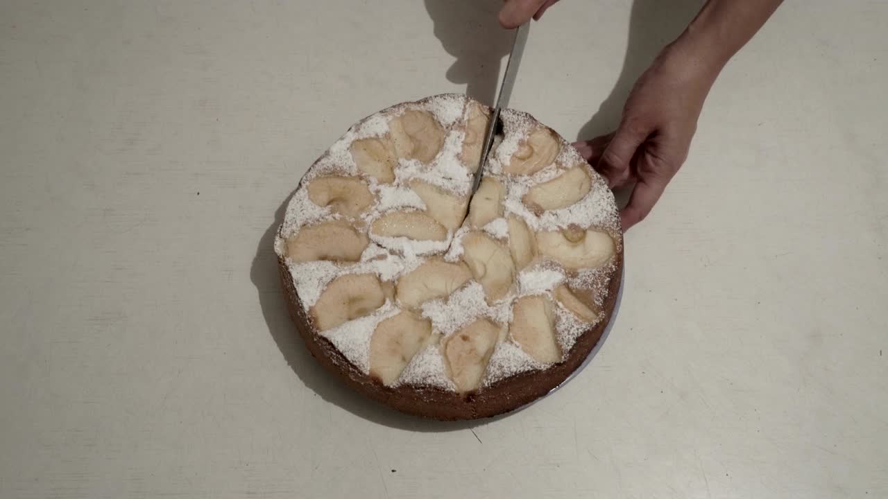 la mujer comienza a cortar un pastel de manzana redondo con un cuchillo grande en pedazos iguales en una mesa blanca en la cocina de la casa. vista superior. de cerca. 4k.