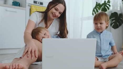 Moderne-Wohnung-Mutter-Und-Zwei-Söhne-Sitzen-Auf-Dem-Boden-Im-Wohnzimmer-Und-Schauen-Auf-Den-Laptop-Bildschirm