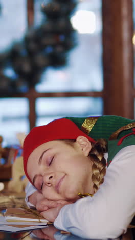 christmas time. elf is sleeping at the table indoors. beautiful elf wakes up after her sleep in the decorated room on festive table background. vertical video