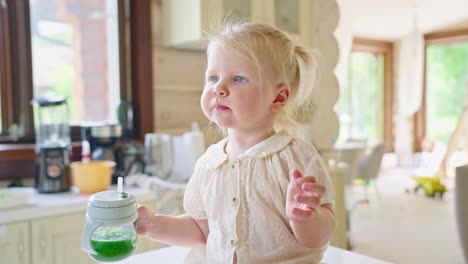 toddler drinking green smoothie in kitchen