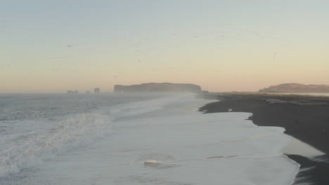 Toma-Aérea-De-Dolly-Forward-Sobre-La-Playa-Islandesa-De-Arena-Negra-Mientras-Los-Pájaros-Vuelan-Por-Encima