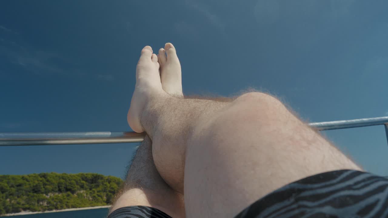 넓은 바다로 순항하는 보트의 레일에서 편안한 남자 다리, pov