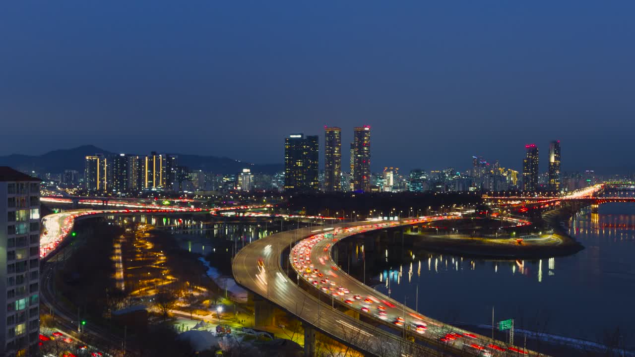 Ampio hyperlapse panoramico aereo di Seoul che passa dal crepuscolo alla notte, con la Lotte World Tower illuminata, il ponte di Seongsu e il traffico scorrevole sull'autostrada Gangbyeonbuk-ro nel 2026