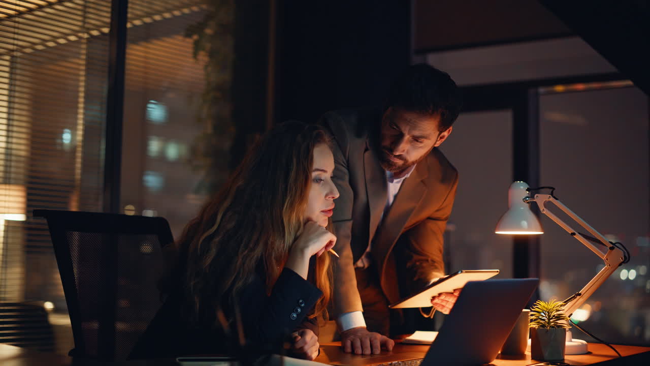 Young entrepreneurs analyzing goals night shift in dark office watching screen