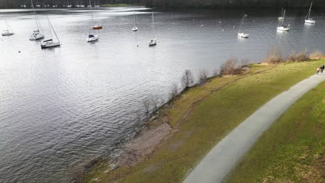 Rising-drone-view-of-sailboats-moored-near-shoreline-of-lake-at-Windermere,-UK