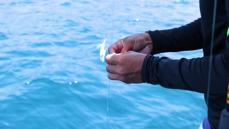 a person prepares fishing bait on a boat in phuket, thailand, with clear blue waters and bright daylight