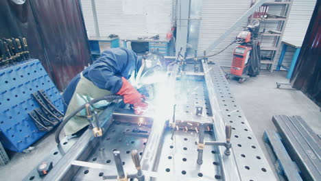 Worker-in-protective-suit-and-mask-conducting-metal-welding.-Factory-welder