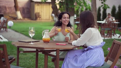 people, communication and friendship concept - smiling young european women drinking orange juice at outdoor cafe, clicking