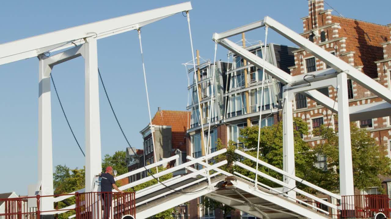 White bascule drawbridge lifts over Haarlem canal, historic Dutch buildings under bright summer daylight