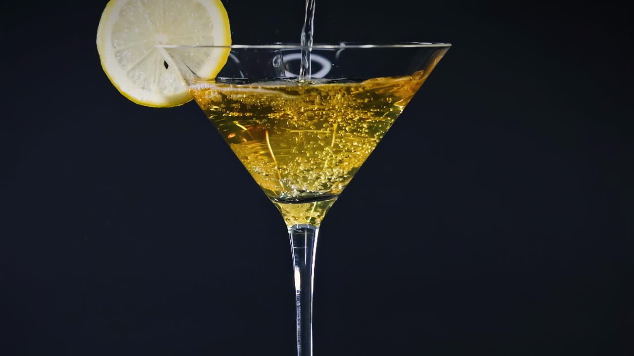 A lemon slice adorns a glass filled with a golden liquid, set against a dark backdrop.