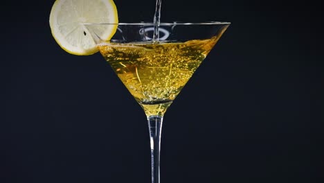 a lemon slice adorns a glass filled with a golden liquid, set against a dark backdrop.
