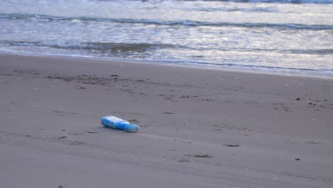 botella de plástico azul en la playa, basura y basura en una playa vacía de arena blanca del mar báltico, problema de contaminación ambiental, tarde tranquila, tiro medio ancho