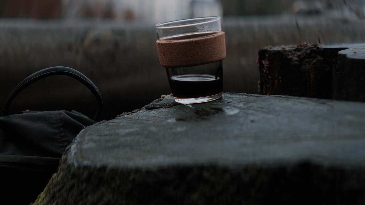 Primo piano di una tazza di caffè su un ceppo di legno all'aperto, nella natura, che viene sollevata. Caffeina mattutina appena preparata in Slow Motion 4K. Paesaggio autunnale