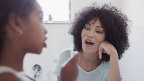 Happy-african-american-mother-and-daughter-brushing-teeth-in-bathroom,-slow-motion