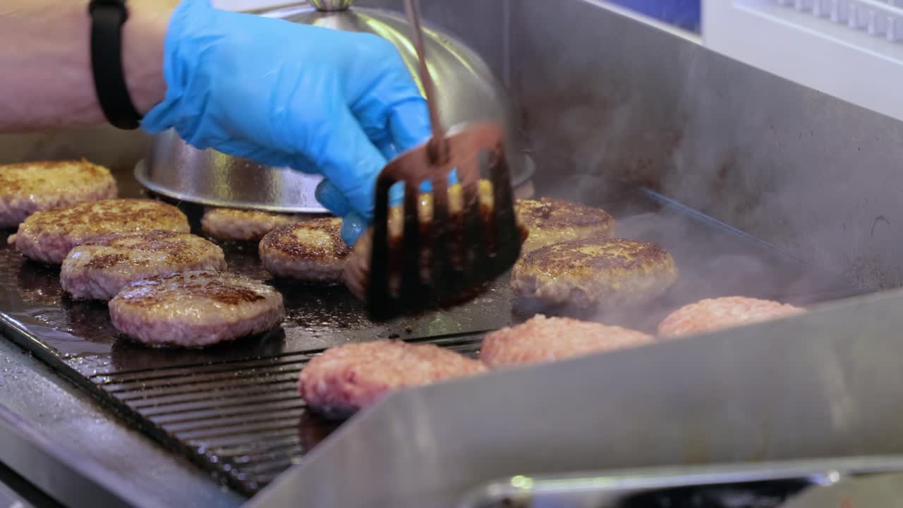 la carne de res se cocina en una sartén caliente. comida callejera, el chef lanza hamburguesas con una espátula.
