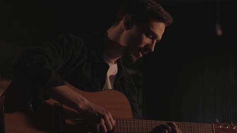 a handsome guy plays an acoustic guitar in an abandoned cinema. the musician sings a song and accompanies on the guitar