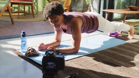 hombre afroamericano en forma sonriente haciendo ejercicio en casa, haciendo abdominales y filmando un vlog de fitness
