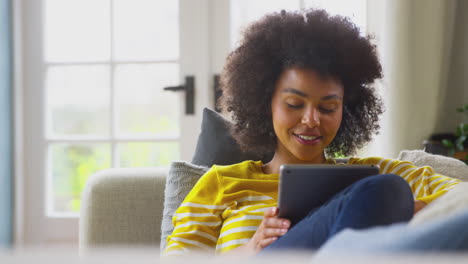 Woman-Relaxing-On-Sofa-At-Home-Using-Digital-Tablet-To-Stream-Movie-Or-Shop-Online