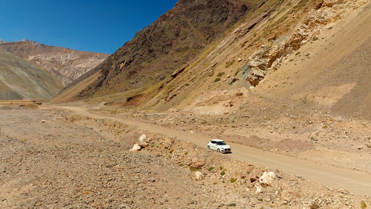 Car driving along road trip through arid Cajón del Maipo canyon, vehicle on dirt road in Andes mountains, Chile. Aerial backward