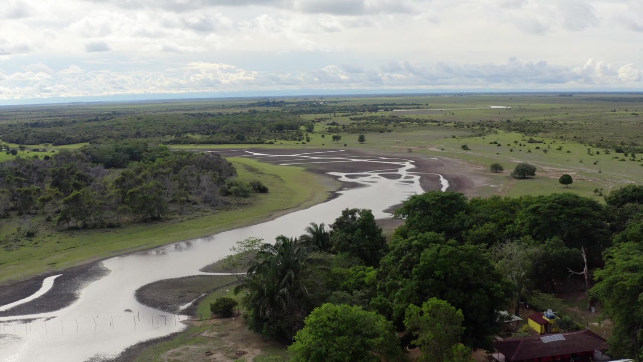Drone shot glides over a winding river, dense forest, and open savanna in the Orinoquía, Colombia. Soft daylight enhances vivid green landscapes.