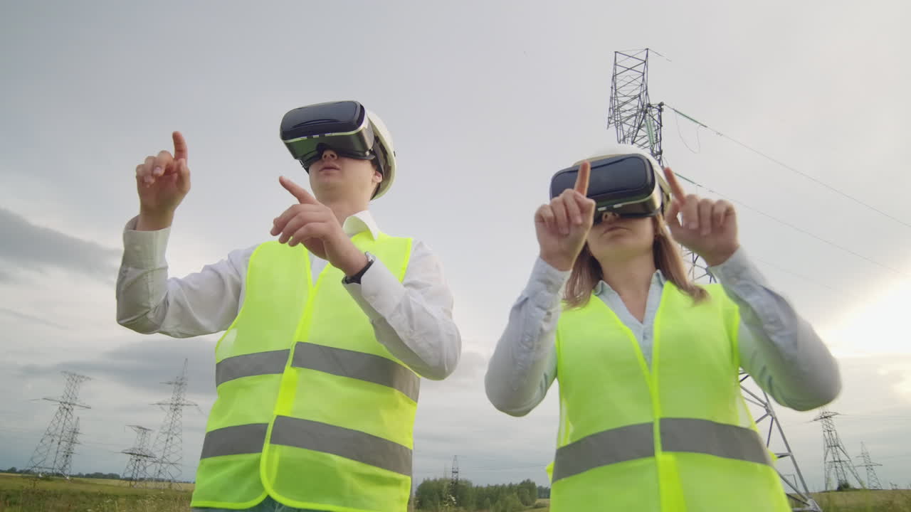 Two engineers of power engineers in VR glasses move their hands simulating the operation of the interface of the control system and planning of high-voltage lines for the delivery of electricity from alternative energy sources.