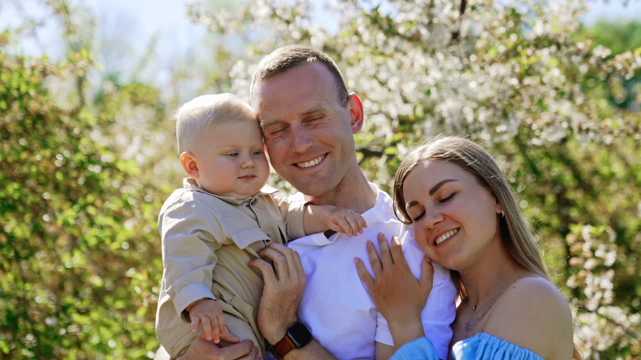 Beautiful Caucasian family of three outdoors on sunny day. Happy parenting concept. Blurred nature at backdrop.