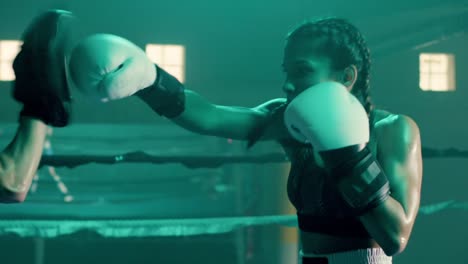 medium shot of a strong caucasian sportswoman training with coach, wearing boxing gloves and punching boxing paws