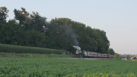 una máquina de vapor de 1924 con un tren de pasajeros que echa humo y viaja a lo largo de la campiña amish en un día de verano