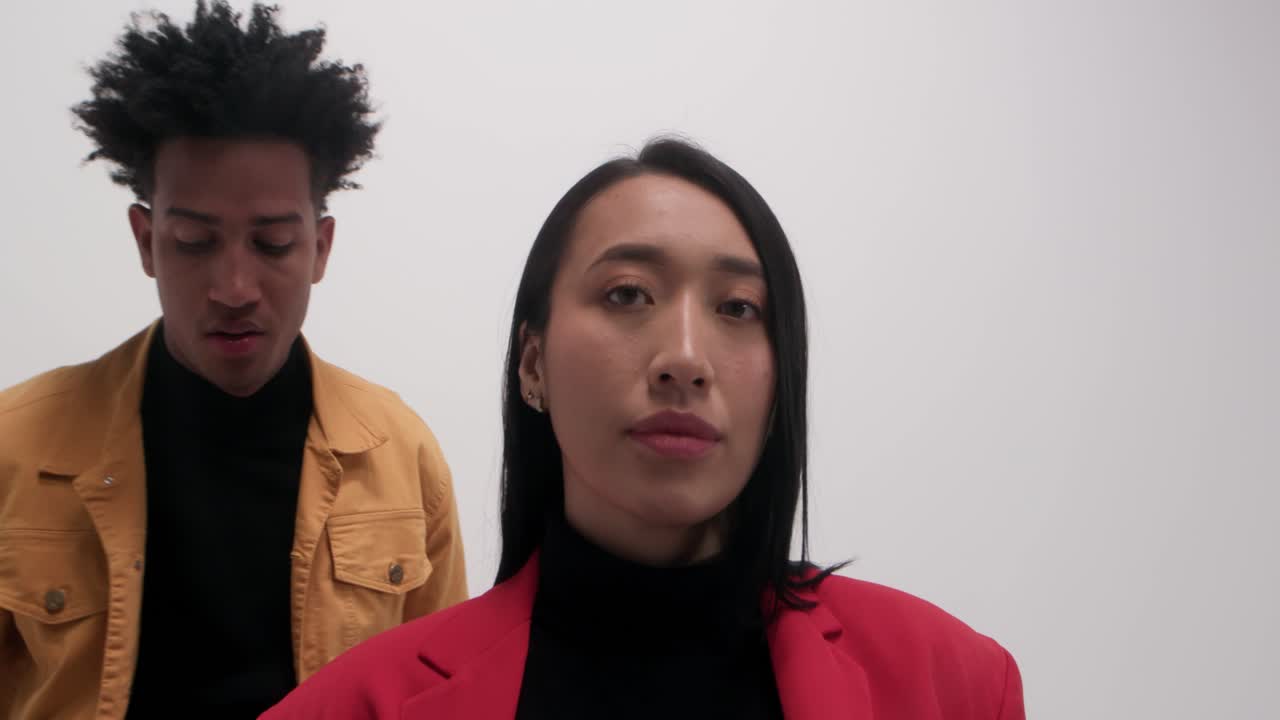 Two diverse young professionals standing back to back in a white studio, confident corporate body language, modern business style, teamwork and inclusion concept