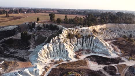 aerial drone shot orbiting around an old eroded gold mine slimes dump, the large mounds of dried disregarded tailings being recycled using modern mining technology, benoni, south africa