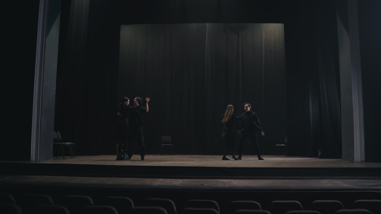 dos parejas de actores activos en trajes negros bailan su baile lento en el escenario durante la preparación para una actuación y ensayo en un teatro vacío