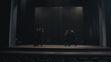 two pairs of active actors in black suits dance their slow dance on stage during preparation for a performance and rehearsal in an empty theater