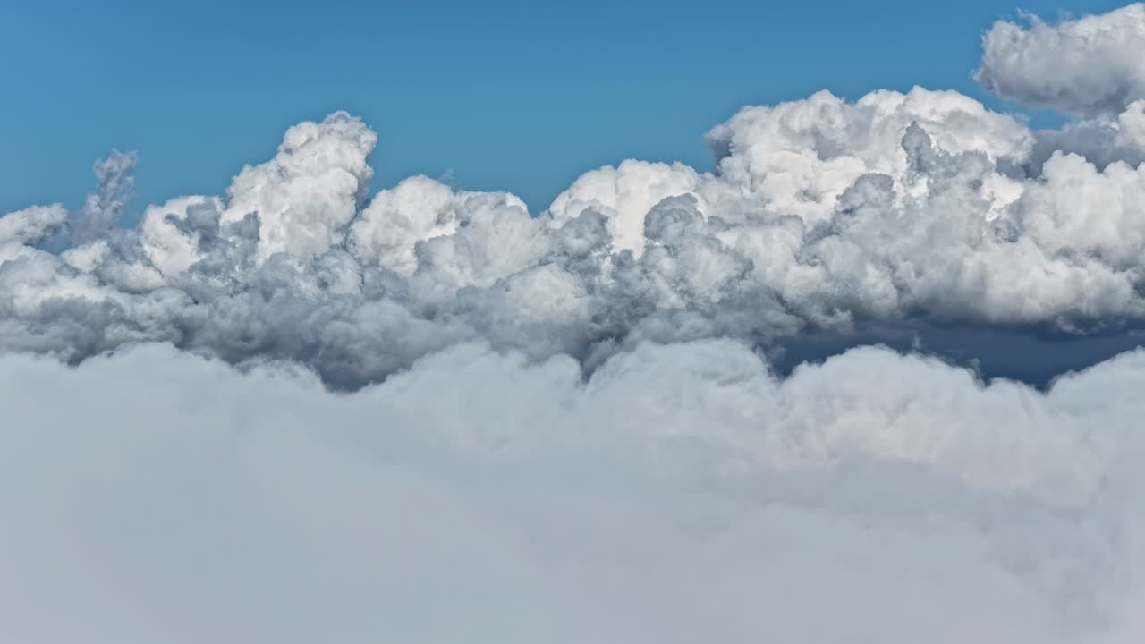 High altitude aerial forward flight above massive voluminous white cumulus clouds with deep blue sky background and dramatic fluffy cloud formations