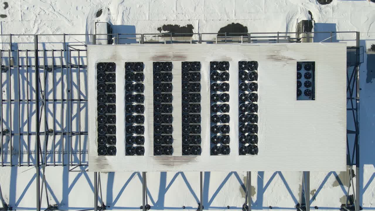 Ascending aerial top view of spinning cooling fans on AI data center rooftop covered in snow, highlighting operational resilience in cold weather