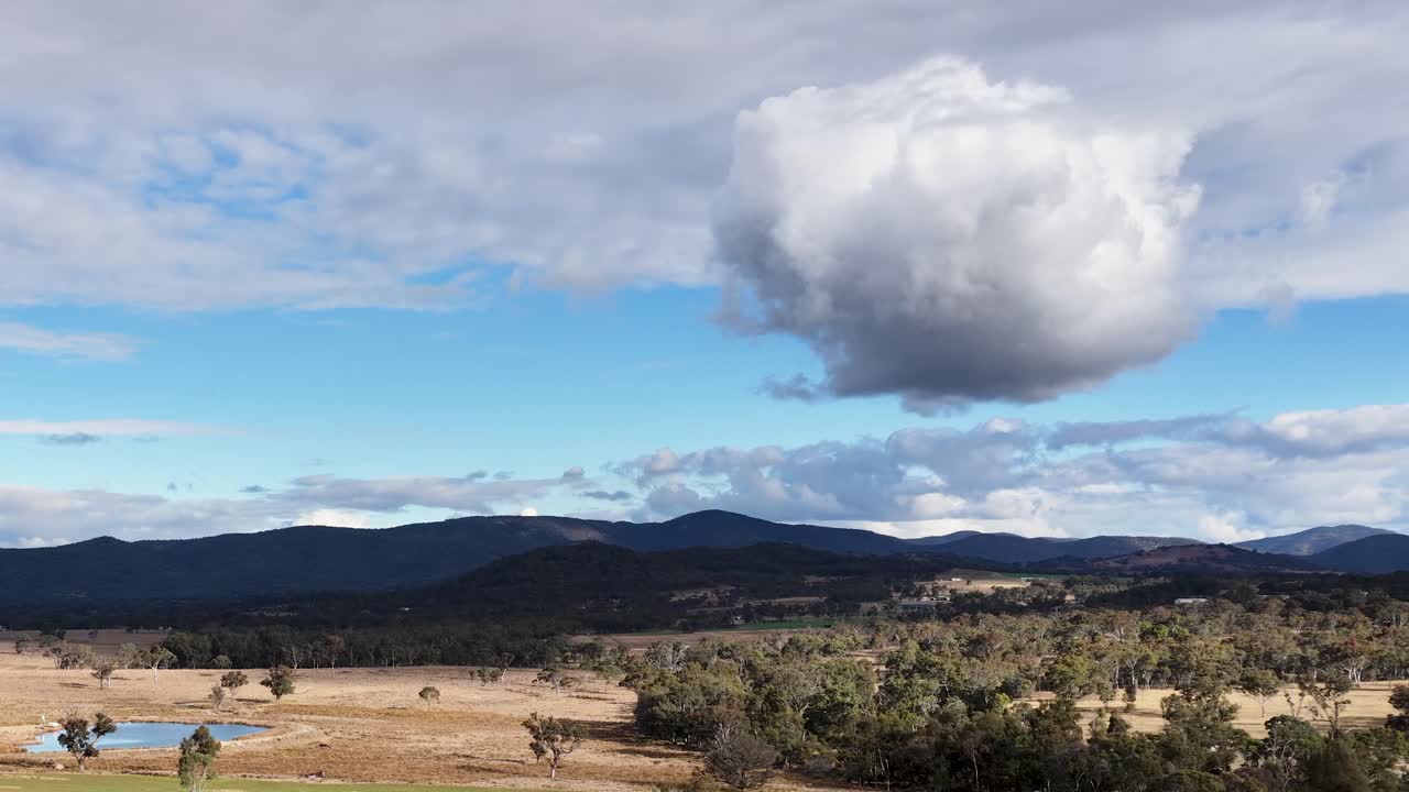 A single large cloud moves across a bright sky above open farmland and distant hills in Stanthorpe, Queensland. Static wide shot, natural daylight